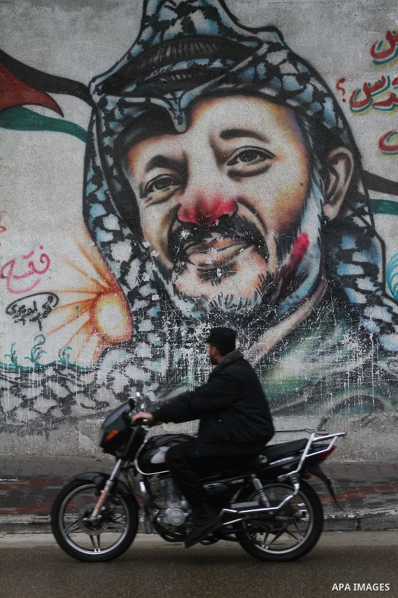 A Palestinian man rides his motorcycle passes by a mural of the Palestinian Leader Yasser Arafat, in Gaza City on January 1, 2011. Palestinians celebrating the 46th anniversary of the founding of the Palestinian National...