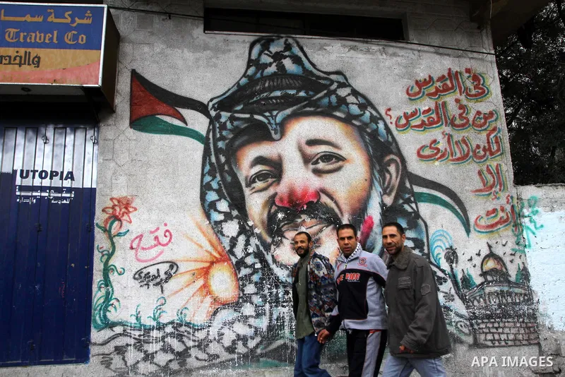 Palestinian men walk in front of a mural of the Palestinian Leader Yasser Arafat, in Gaza City on January 1, 2011. Palestinians celebrating the 46th anniversary of the founding of the Palestinian National Liberation Move...