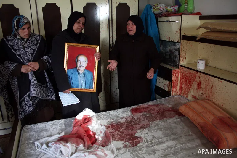 The wife of 67-year-old Omar Kawasme stands near his picture and his blood-stained bed where she said he was killed by Israeli troops on January 7, 2010 in Hebron during a raid to arrest suspected militants. The shooting...