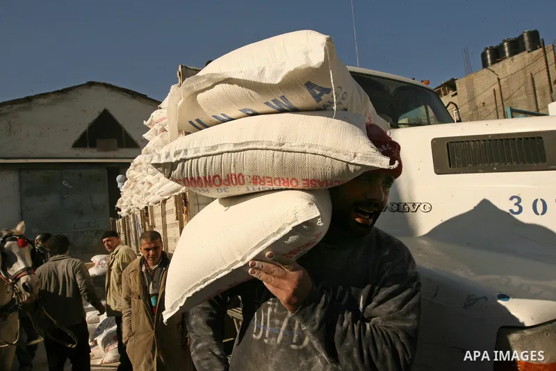 Palestinian man carries a bag with wheat flour on his shoulders as he walks near an UN distribution car at the refugee camp of Rafah in the southern Gaza Strip on January 13, 2011. The UN distribution center is one of ma...