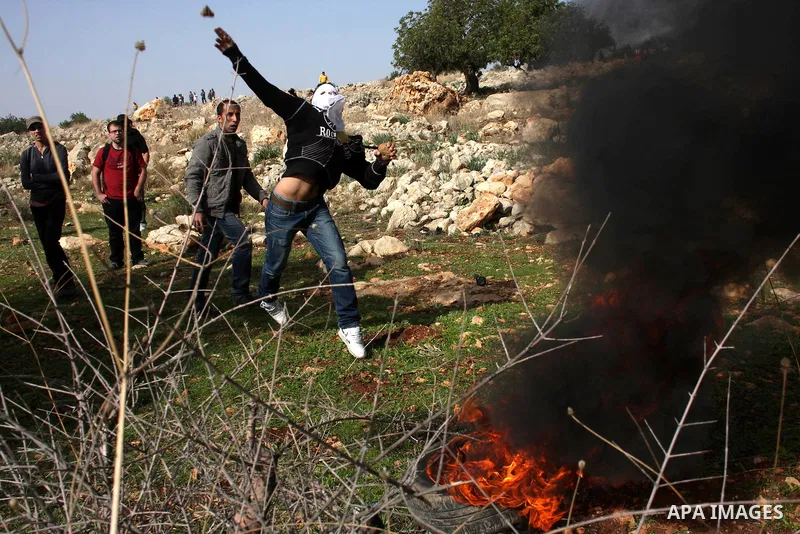A Palestinian protester hurls a stone at Israeli troops, during a protest against Israel's separation barrier in the West Bank village of Nilin near Ramallah, Friday, Jan. 14, 2011. Photo by Issam Rimawi