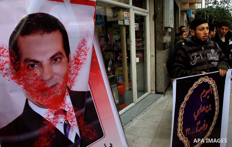 A Palestinian man stands past a poster with a picture of Tunisia's former President Zine al-Abidine Ben Ali as he hold a poster during a Hamas rally in Gaza City to show support for the Tunisian people on January 16, 201...