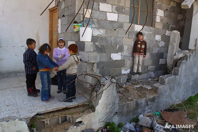 Palestinian children play outside their home which were partially destroyed during the Israeli war on Gaza as Palestinian Prime Minister in Gaza, Ismail Haniyeh delivers a speech during the launching ceremony and placing...