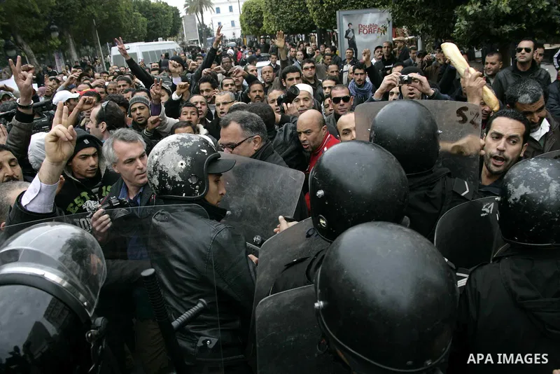 Protestors hold bread as they face riot police officers during a demonstration against the Constitutional Democratic Rally, RCD, party of Ben Ali in the center of Tunis, Tuesday, Jan. 18. 2011. Four ministers quit Tunisi...
