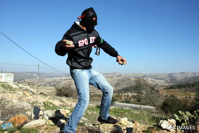 A Palestinian protester hurls stones towards Israeli soldiers during a demonstration against the expansion of the nearby Jewish settlement of Halamish in the West Bank village of Nabi Saleh, near Ramallah, Friday, Jan. 2...