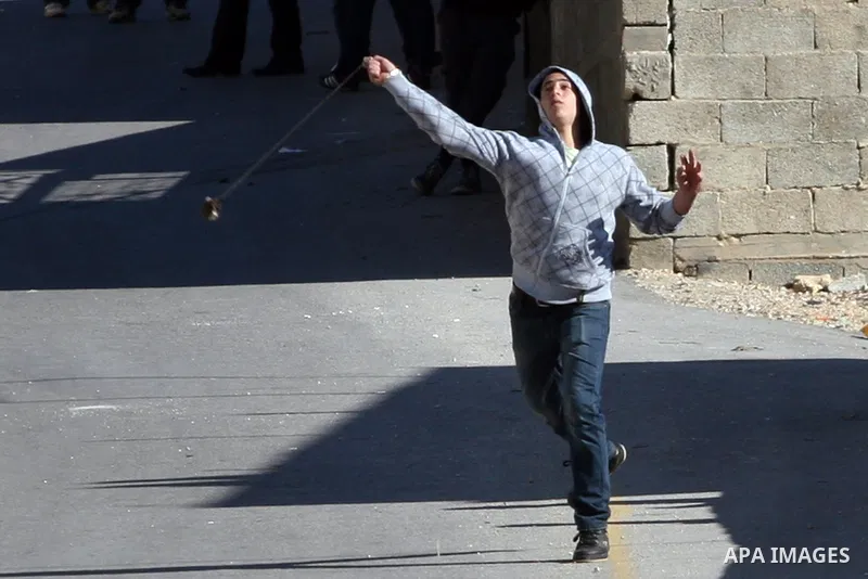 A Palestinian protester hurls stones towards Israeli soldiers during a demonstration against the expansion of the nearby Jewish settlement of Halamish in the West Bank village of Nabi Saleh, near Ramallah, Friday, Jan. 2...