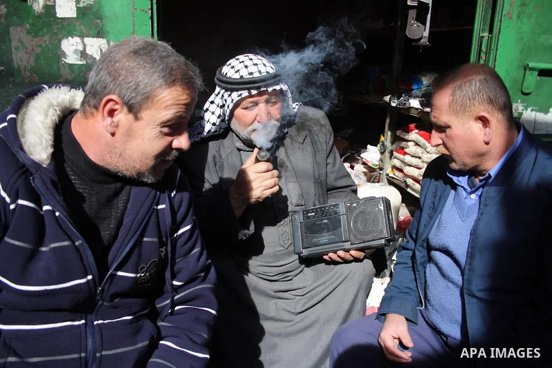 Palestinian men listen to the Radio in front of his shop in the West Bank city of Hebron on 24 January 2011 concerning the 1,600 secret documents published by Al-Jazeera about the Israeli Palestinian negotiations. Palest...
