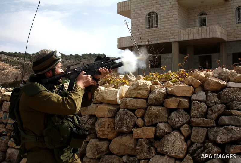 Israeli soldier fires tear gas at Palestinian stone throwers during a demonstration by Palestinians against the demolishing of farm land to be used in the construction of Jewish settlements near the existing Israeli sett...