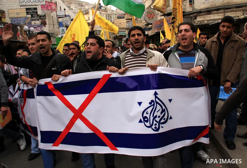 Palestinians hold Al-Jazeera logos printed in an Israeli flag during a rally in the West Bank City of Nablus , to protest against Al-Jazeera TV Channel on 27 January 2011. Al-Jazeera, a Qatar-based Arab satellite station...