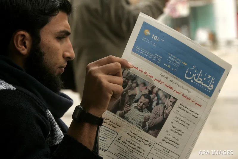 A Palestinian youth reads a local newspaper in front of his shop to follow up the latest developments in Egypt, in the southern Gaza Strip town of Rafah on Feb. 1, 2011. Photo by Abed Rahim Khatib