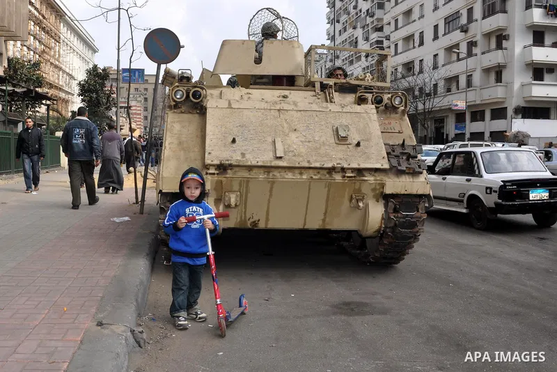 A boy stands next a tank during demonstrations in Tahrir Square in downtown Cairo, Egypt, Tuesday, Feb. 8, 2011. Protesters appear to have settled in for a long standoff, turning Tahrir Square into a makeshift village wi...