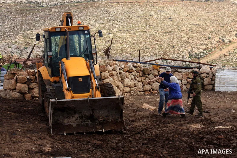 A Palestinian woman gestures as she stands facing a bulldozer of the Civil Administration during a demolition in the village of Khirbet Tana near the West Bank city of Nablus, Wednesday, Feb. 9, 2011. According to Palest...