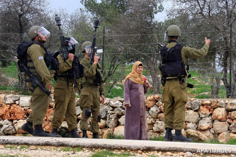 A Palestinian woman stands next Israeli soldiers and border police standig guards during the weekly demonstration against Israel's separation barrier in the West Bank village of Bilin near Ramallah, Friday, Feb. 11, 2011...