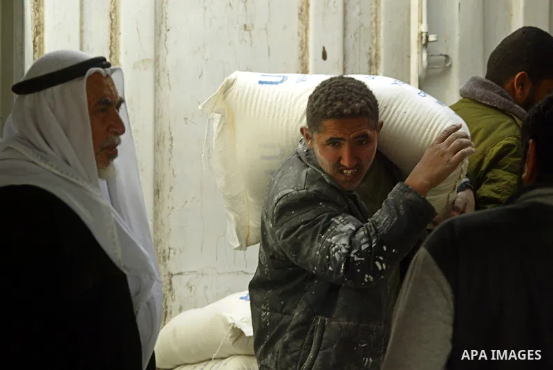 Palestinian youth carries a bag with wheat flour on his shoulders as others receive food aids from the United Nations Relief and Works Agency (UNRWA) at the Rafah refugee camp, in the southern Gaza Strip on February 16,...