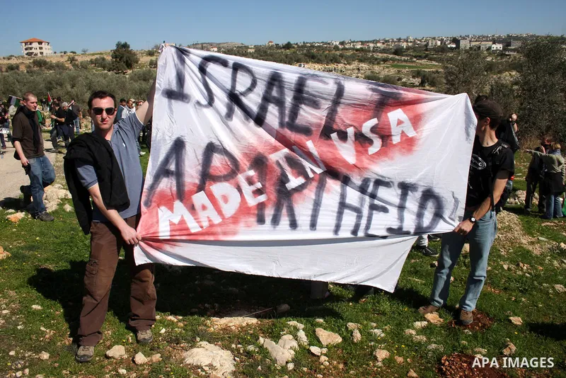 Protesters hold signs during the weekly demonstration against Israel's separation barrier in the West Bank village of Bilin near Ramallah, Friday, Feb. 18, 2011. Photo by Issam Rimawi