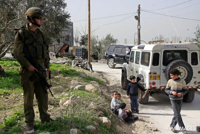 An Israeli soldier next to boys in the village of Jeet the West bank city of Qalqilya, Friday,25, 2011. Palestinians and the Israeli military said Friday Jewish settlers vandalized in a Palestinian village in the West Ba...