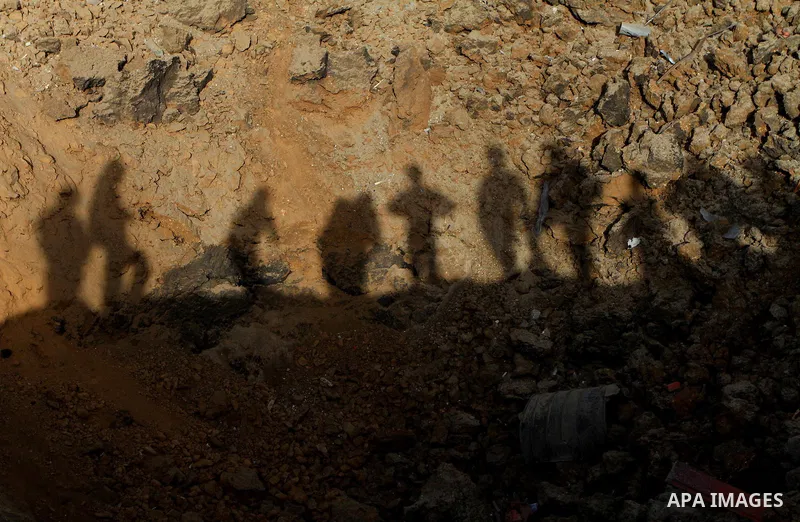 The shadows of Palestinians are cast on a crater left after a missile fired from an Israeli warplane hit Nusairat refugee camp, Central Gaza strip, Saturday, Feb. 26, 2011. The Israeli airforce attacked Friday night seve...