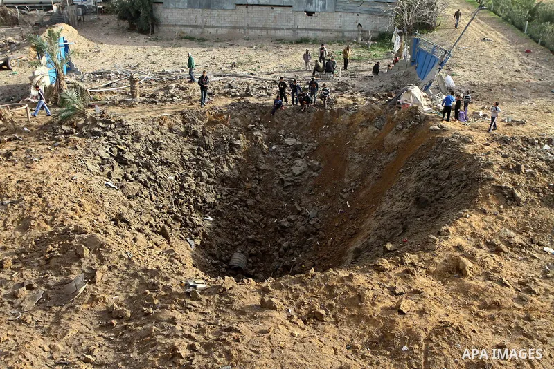 Palestinians stand next to a crater left after a missile fired from an Israeli warplane hit Nusairat refugee camp, Central Gaza strip, Saturday, Feb. 26, 2011. The Israeli airforce attacked Friday night several targets i...