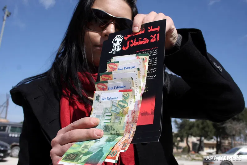 A Palestinian activist holds News Israeli Shekels' bills marked with stickers reading "Free Palestine" on March 7, 2011 in the West Bank city of Ramallah, as part of a campaign aimed to peacefully express opposition to I...