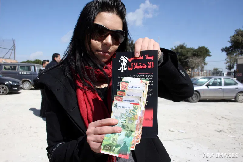 A Palestinian activist holds News Israeli Shekels' bills marked with stickers reading "Free Palestine" on March 7, 2011 in the West Bank city of Ramallah, as part of a campaign aimed to peacefully express opposition to I...