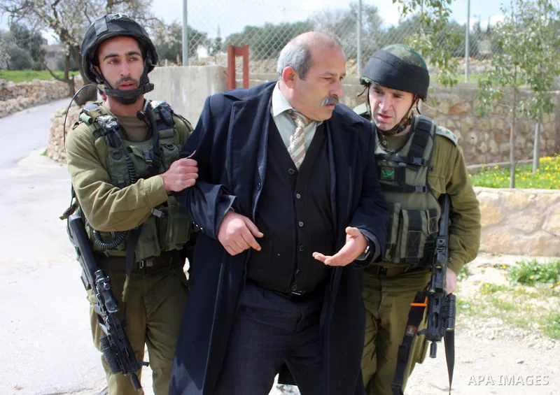 Israeli soldiers arrest a demonstrator as Palestinian men (not seen ) wave their national flag as they sit and block Road 60, which links Jerusalem and Hebron and is used by both Palestinians and Jewish settlers, on Marc...