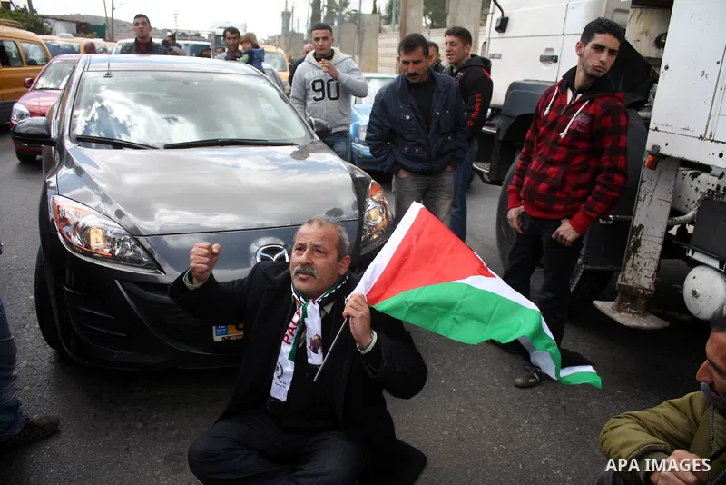 Palestinian men wave their national flag as they sit and block Road 60, which links Jerusalem and Hebron and is used by both Palestinians and Jewish settlers, on March 08,2011 in Beit Omar near the West Bank city of Hebr...