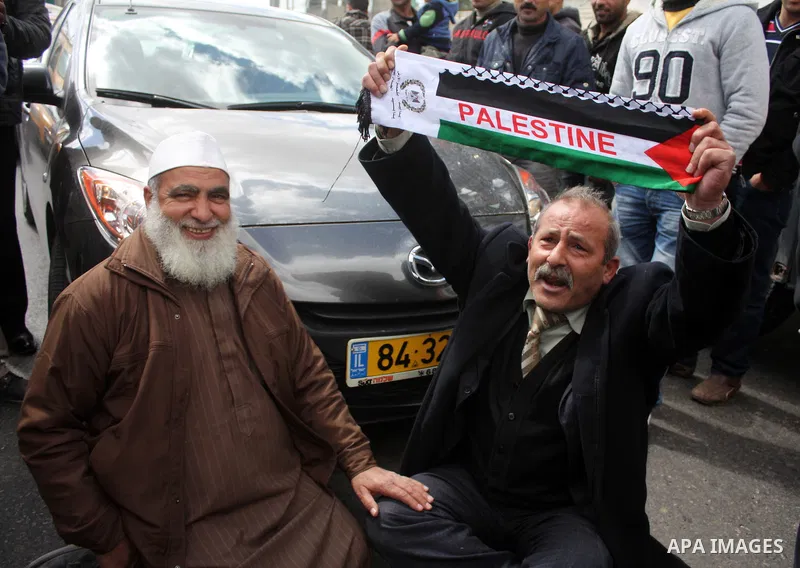 Palestinian men wave their national flag as they sit and block Road 60, which links Jerusalem and Hebron and is used by both Palestinians and Jewish settlers, on March 08,2011 in Beit Omar near the West Bank city of Hebr...