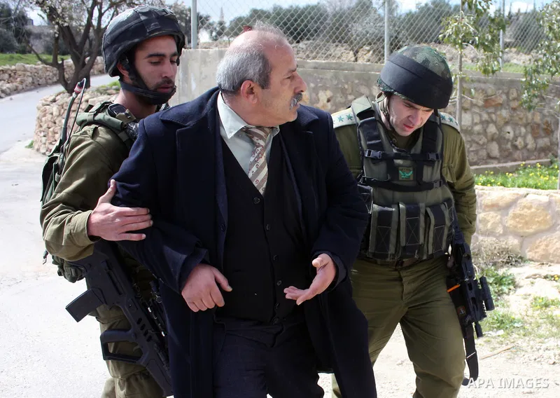 Israeli soldiers arrest a demonstrator as Palestinian men (not seen ) wave their national flag as they sit and block Road 60, which links Jerusalem and Hebron and is used by both Palestinians and Jewish settlers, on Marc...