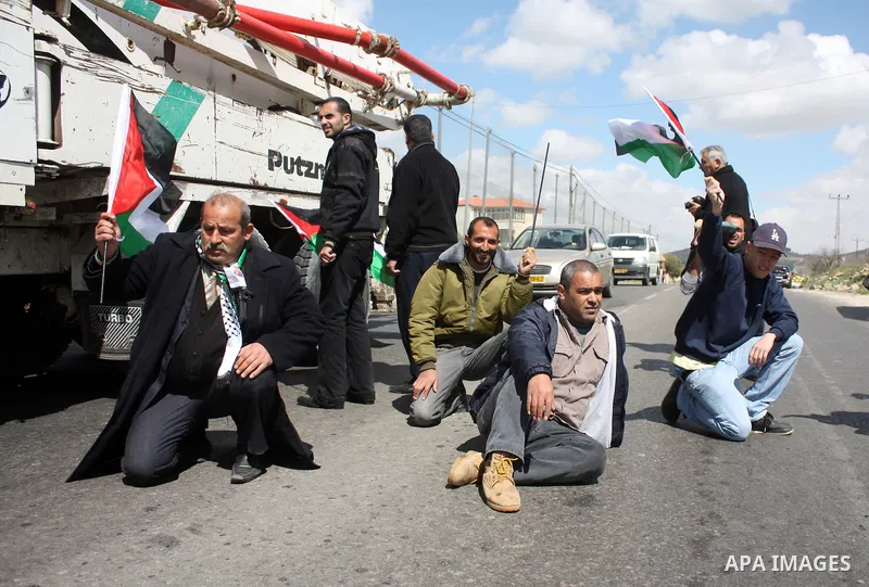 Palestinian men wave their national flag as they sit and block Road 60, which links Jerusalem and Hebron and is used by both Palestinians and Jewish settlers, on March 08,2011 in Beit Omar near the West Bank city of Hebr...
