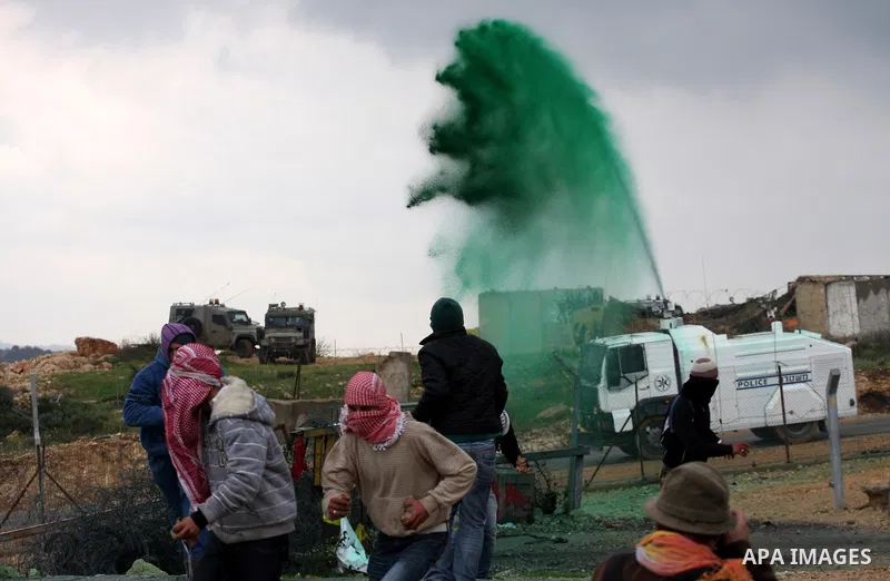 Palestinian protesters run a way as colored water is sprayed by the Israeli army from a water canon during the weekly demonstration against Israel's controversial separation barrier in the village of Bilin, near the West...
