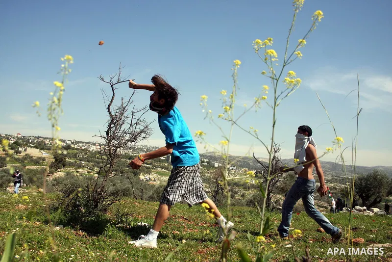 Palestinian youths throw stones at Israeli forces during clashes following a weekly demonstration against Israel's separation barrier in the West Bank village of Bilin on March 18, 2011. Photo by Issam Rimawi