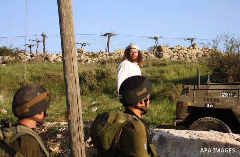 Israeli soldiers stand guard near Israeli settlers from the Kharsina settlement as they prevent settlers from throwing stones at Palestinian cars on March 21,2011 near Hebron in the Israeli-occupied West Bank, as three P...