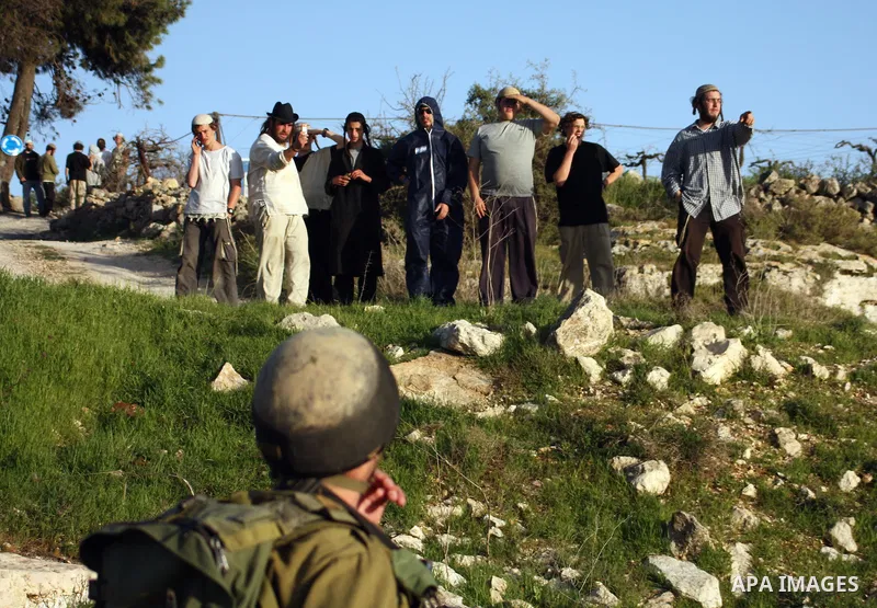Israeli soldiers stand guard near Israeli settlers from the Kharsina settlement as they prevent settlers from throwing stones at Palestinian cars on March 21,2011 near Hebron in the Israeli-occupied West Bank, as three P...
