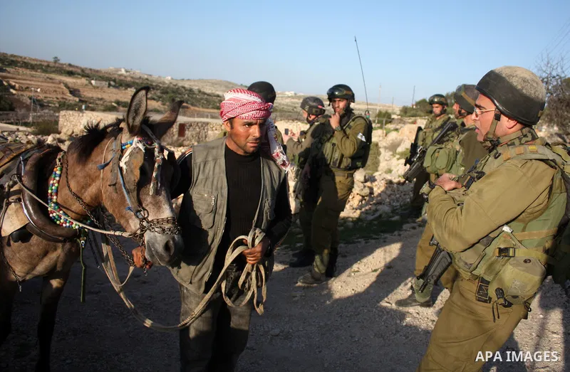 Israeli soldiers stand guard near Israeli settlers from the Kharsina settlement as they prevent settlers from throwing stones at Palestinian cars on March 21,2011 near Hebron in the Israeli-occupied West Bank, as three P...