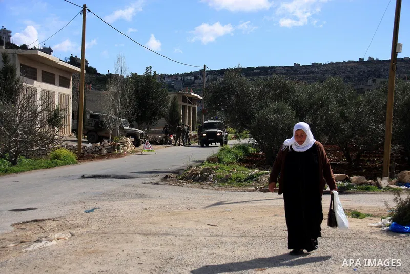 Palestinian woman walks next to an Israeli military checkpoint during a military operation searching for suspects in the West Bank village of Awarta near Nablus,the Impose a curfew in the village in following a Palestini...