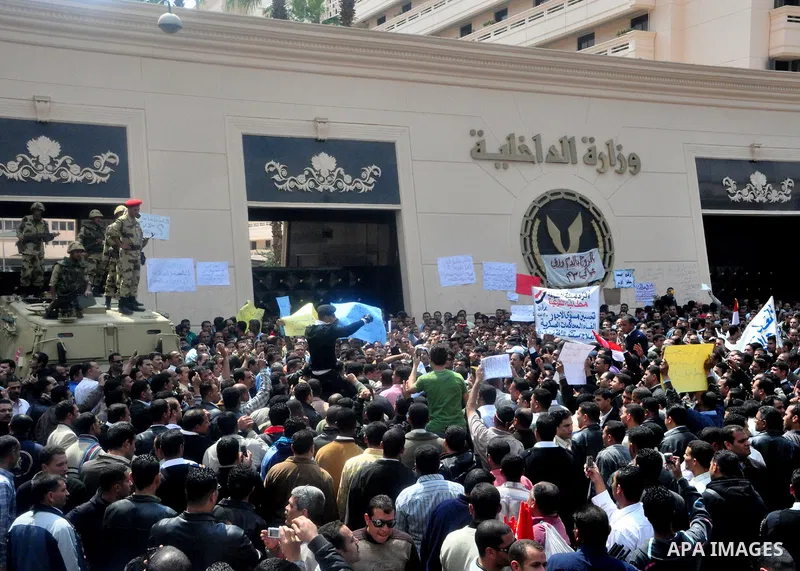 Egyptian police protest in front of the Interior Ministry, calling for a raise in their wages, as army soldiers stand guard atop their armored vehicle in Cairo, Egypt, Tuesday, March 22, 2011. The Arabic on building read...