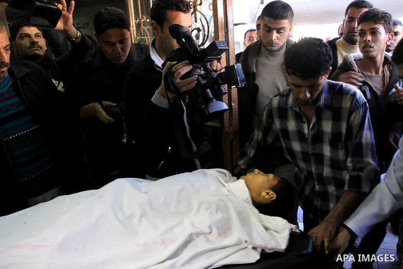 Palestinians stand next to the body of a Palestinian killed in an Israeli shells, after was brought to the morgue of Shifa hospital in Gaza City, Tuesday, March 22, 2011. Israeli tank fire struck a house in the Gaza Stri...