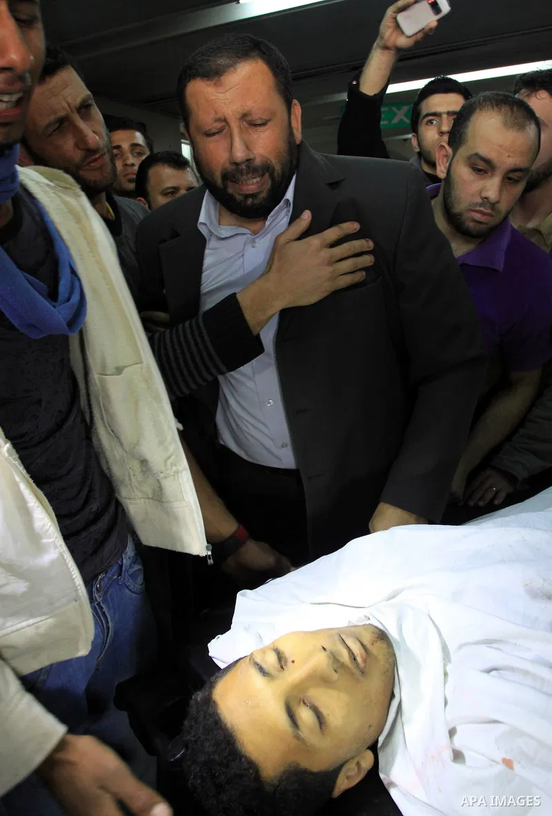 Palestinians stand next to the body of a Palestinian killed in an Israeli shells, after was brought to the morgue of Shifa hospital in Gaza City, Tuesday, March 22, 2011. Israeli tank fire struck a house in the Gaza Stri...