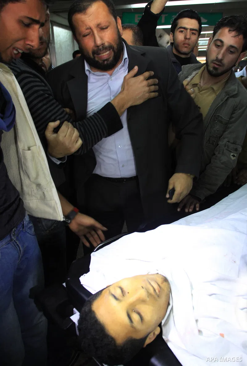 Palestinians stand next to the body of a Palestinian killed in an Israeli shells, after was brought to the morgue of Shifa hospital in Gaza City, Tuesday, March 22, 2011. Israeli tank fire struck a house in the Gaza Stri...