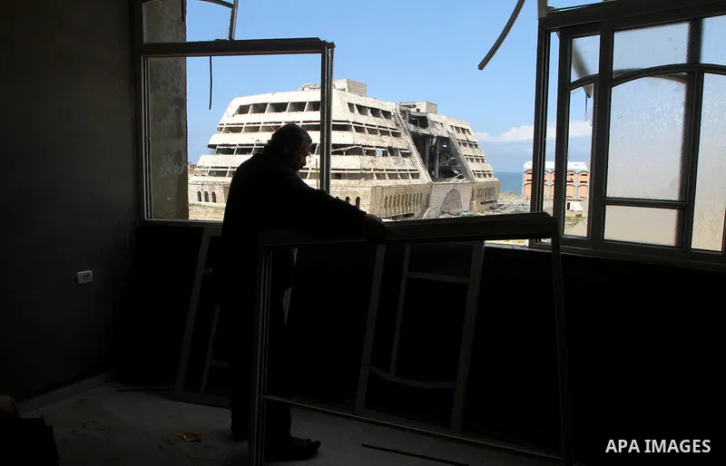 A Palestinian adjusts his broken windows in front of destroyed security office in Gaza City, on March 25, 2011, as Israeli aircraft attacked four targets in the Gaza Strip during the night, lightly wounding three people,...