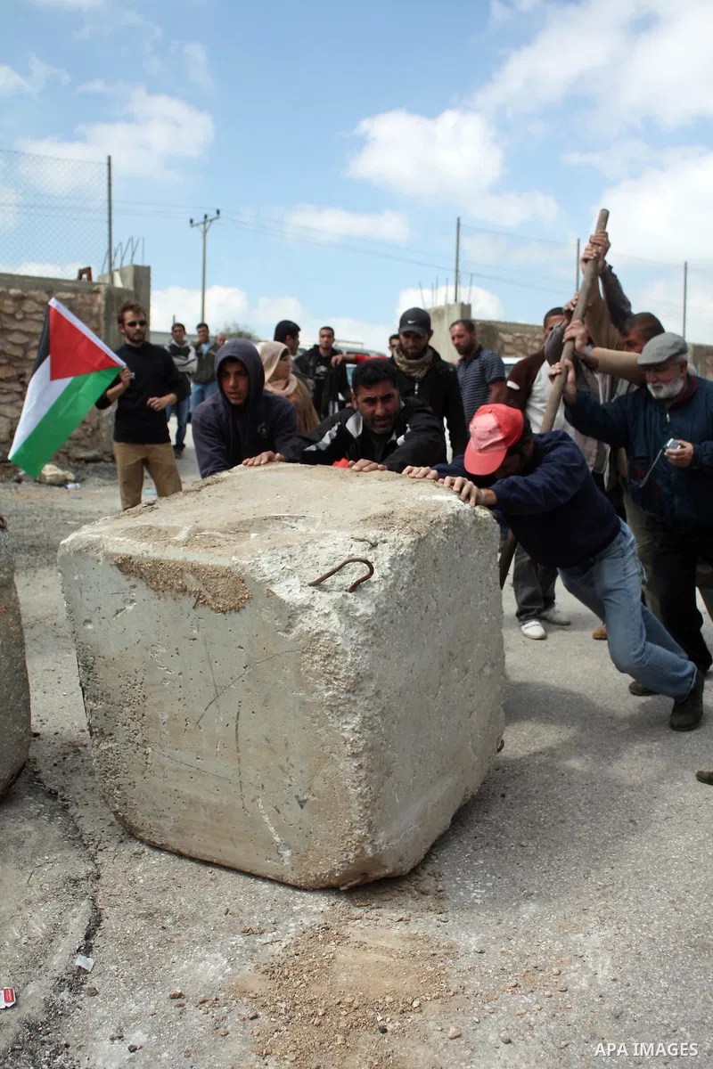 Palestinian, Israeli and foreign peace activists use a metal to move a boulder blocking a road close to a entry point into the Palestinian West Bank village of Beit Omar northen the West Bank city of Hebron on March 26,2...