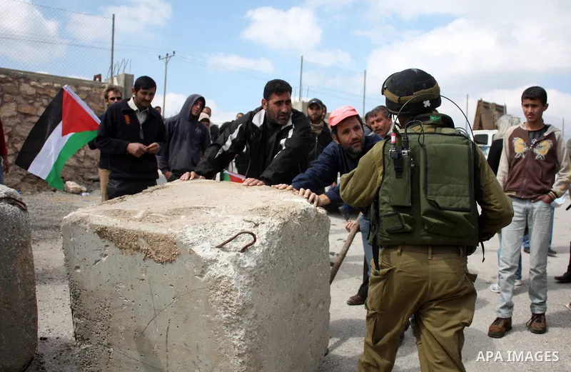 Palestinian, Israeli and foreign peace activists use a metal to move a boulder blocking a road close to a entry point into the Palestinian West Bank village of Beit Omar northen the West Bank city of Hebron on March 26,2...