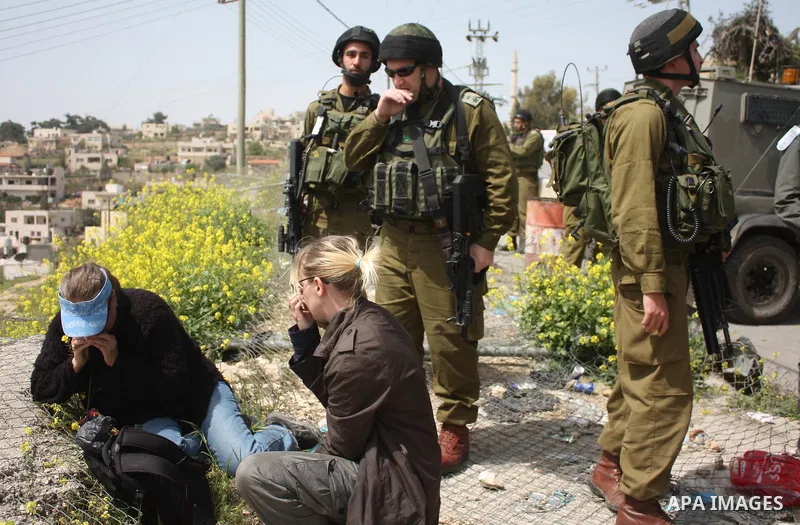 Demonstrators sit on a fence during a protest by foreign, Israeli and Palestinian demonstrators against the controversial Israeli separation barrier, in the Palestinian village of Beit Omar, near the West Bank city of He...