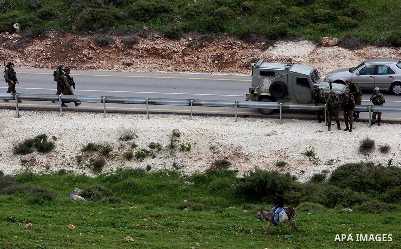 A Palestinian youth rides his donkey past Israeli soldiers standing guard during a demonstration against the expansion of the nearby Jewish settlement of Halamish in the West Bank village of Nabi Saleh near Ramallah, Sat...
