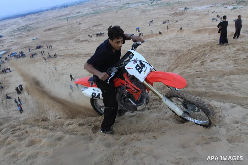 A Palestinian man rides his motorcycle on sand dunes during the weekly sport event in the Gaza Strip town of al-Zahra, south of Gaza City, on April 1,2011. Palestinian youths use the dunes for riding their motorcycles, h...