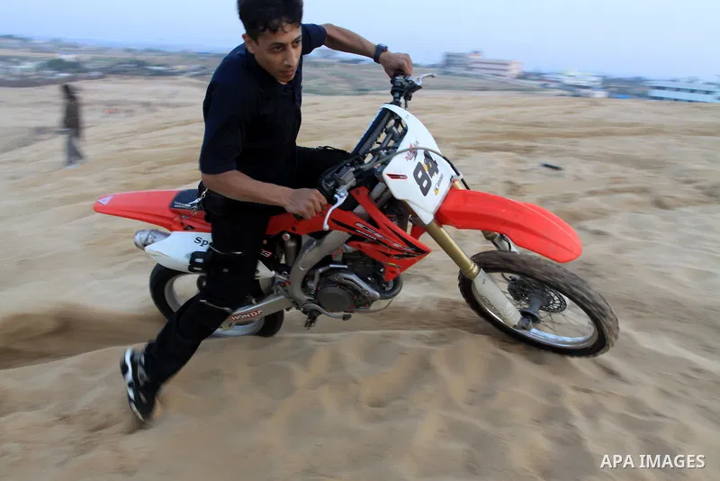 A Palestinian man rides his motorcycle on sand dunes during the weekly sport event in the Gaza Strip town of al-Zahra, south of Gaza City, on April 1,2011. Palestinian youths use the dunes for riding their motorcycles, h...