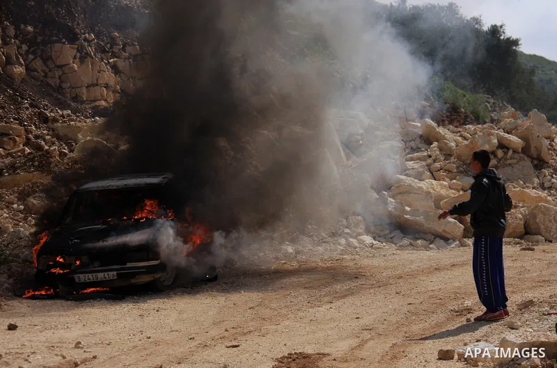 A Palestinian youth walks next to a burning vehicle residents said was torched by Jewish settlers in the West Bank village of Aseera, Saturday, April 9, 2011. Palestinian witnesses said about 40 settlers entered the vill...