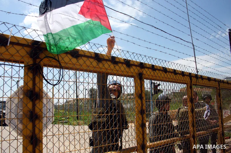 An Israeli soldier removes a Palestinian flag hung on the barbed wire around the gate of the Israeli-controlled Ofer jail during a protest by Palestinians calling for the release of prisoners in the West Bank city of Ram...
