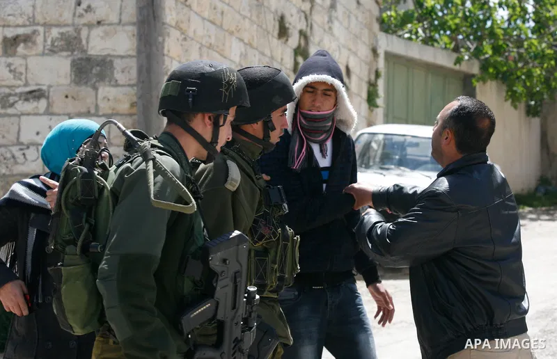Palestinians assist a man as an Israeli soldier tries to arrest him during a military operation searching for suspects during a curfew in the West Bank village of Awarta, near Nablus City on 12 April 2011 as the northern...