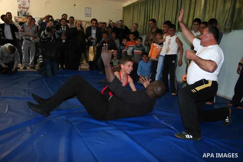 Former French football player Lilian Thuram plays with a Palestinian boy and a referee following a wrestling game at the Tareq Ben Ziad Club in the West Bank city of Hebron on April 13, 2011. Thuram is visiting the Pales...